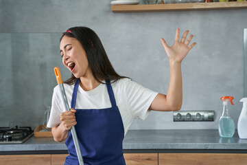 Have fun. Portrait of joyful young woman, cleaning lady pretending to sing, holding broom while...
