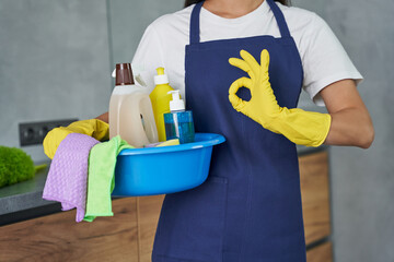 Best products. Cropped shot of cleaning lady showing ok sign while holding container full of...