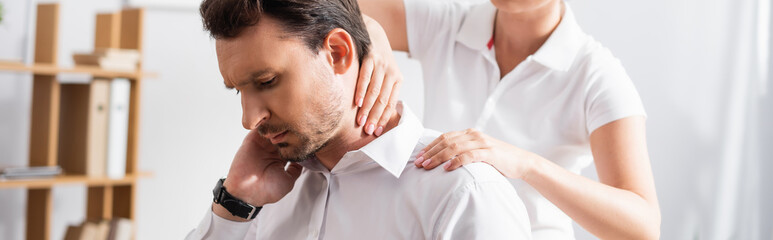 Female massage therapist massaging hurting neck of businessman on blurred background, banner