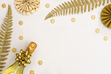 Festive white background with gold decoration , bottle of sparkling wine and paper christmas tree decorations , glittering snowflakes and shiny golden fern leaves, flat lay, top view, copy space