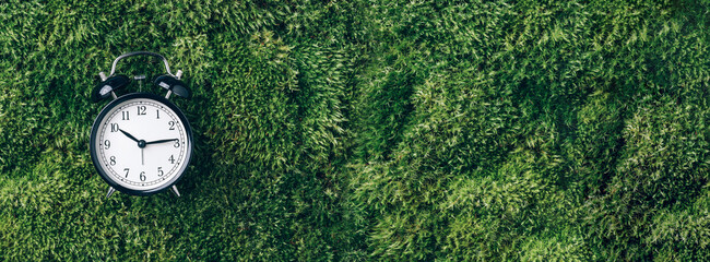 Alarm clock on green grass, moss background. Top view. Copy space. Ecology of sleeping. Banner