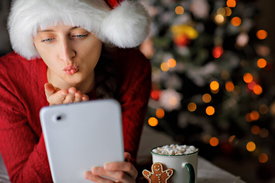 A young girl in a bright red sweater and Santa hat blows a kiss to the interlocutor.