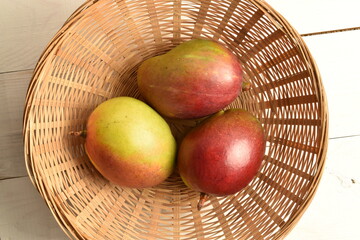 Three organic mangoes in a bowl of wicker vines, close-up.