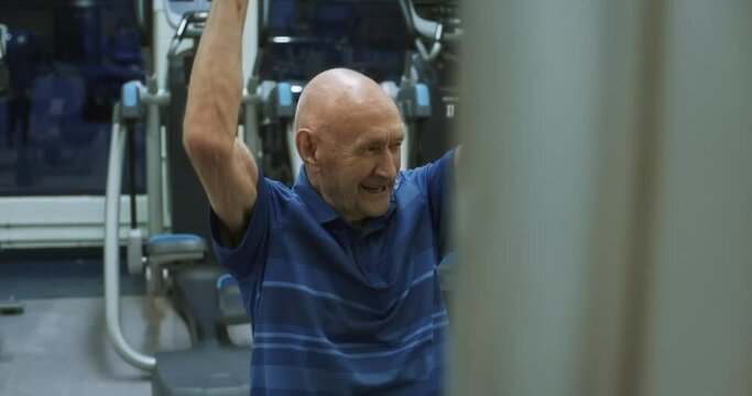 Medium shot, elderly man pulls down weights at gym
