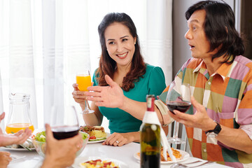 Happy mature Asian couple telling exciting story guests when eating dinner