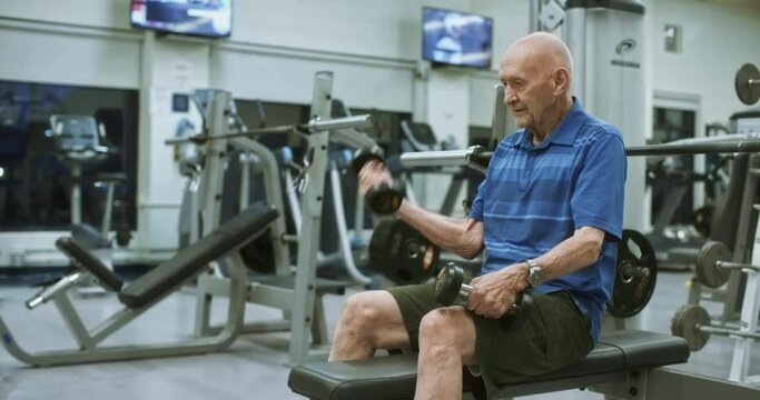 Elderly man lifts two dumbbells at gym, medium shot