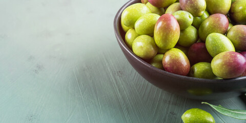 Freshly picked raw green olives in black bowl.