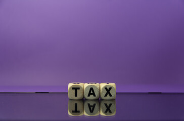 The word tax written with real wooden dices reflecting on a mirror on a purple background