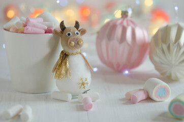 White cup with marshmallows and a toy bull on a blurred background.