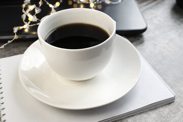 On a wooden table is a Notepad on which there is a white Cup of coffee on the background of a...