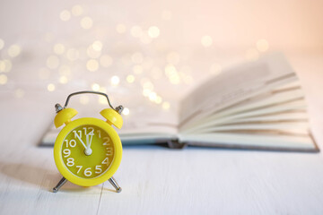 Yellow alarm clock and book on a white table.