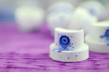 The soiled blue nozzles from the paint sprayer lies on a purple plank on a background of a many...