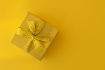 Yellow gift box with a gold ribbon on a yellow background. Gift for birthday, Christmas, mother's Day, Valentine's Day. Top view, horizontal position, copy space