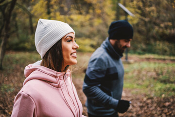 Sporty happy couple in warm outfit jogging in woods at autumn. Selective focus at woman.