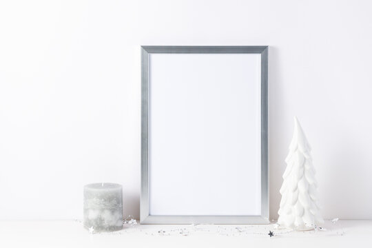 Photo or poster mockup with a silver frame, small decorative ceramic christmas tree  and candle on white