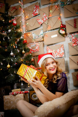 happy smiling girl in Christmas red hat with gifts near decorated new year tree