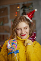 happy smiling girl in red christmas hat with lollipop near decorated christmas tree