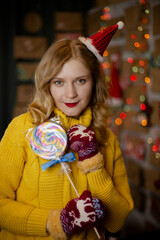 happy smiling girl in red christmas hat with lollipop near decorated christmas tree