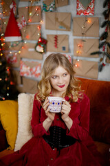 Young woman relaxing at home, enjoying Christmas time. Beautiful girl drinking tea at home, sitting near christmas tree.