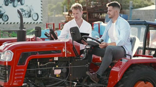Young agronomist with elegant salesman choosing a tractor for farming on the open ground of agricultural shop. The buyer and seller are discussing a machinery.
