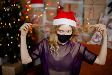 Portrait of a beautiful girl in medical mask, standing in front of decorated christmas tree at home