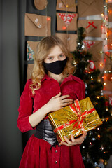 Portrait of a beautiful girl in medical mask, standing in front of decorated christmas tree at home