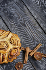 Baked cinnabons in shape. Stand on black composite boards. Nearby are cinnamon sticks. Close-up shot.