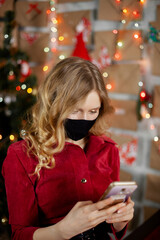 Portrait of a beautiful girl in medical mask, standing in front of decorated christmas tree at home