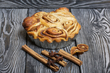 Baked cinnabons in shape. Stand on black composite boards. Nearby are cinnamon sticks. Close-up shot.