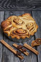 Baked cinnabons in shape. Stand on black composite boards. Nearby are cinnamon sticks. Close-up shot.