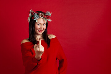 mock up of a laughing Asian young woman in a Christmas wreath showing a fuck, or middle finger, on a red background.
