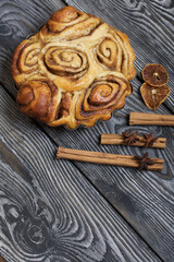 Baked cinnabons in shape. Stand on black composite boards. Nearby are cinnamon sticks. Close-up shot.