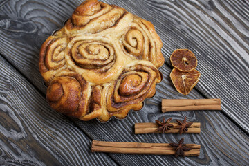 Baked cinnabons in shape. Stand on black composite boards. Nearby are cinnamon sticks. Close-up shot.