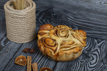 Baked cinnabons in shape. Stand on black composite boards. Nearby are cinnamon sticks. Close-up shot.