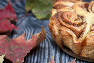 Baked cinnabons in shape. Stand on black composite boards. Nearby are autumn maple leaves.