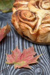 Baked cinnabons in shape. Stand on black composite boards. Nearby are autumn maple leaves.