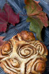 Baked cinnabons in shape. Stand on black composite boards. Nearby are autumn maple leaves.