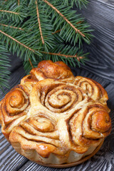 Baked cinnabons in shape. Stand on black pine planks. Nearby there were spruce branches. Close-up shot.