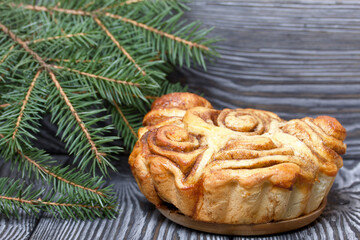Baked cinnabons in shape. Stand on black pine planks. Nearby there were spruce branches. Close-up shot.