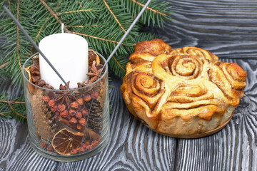Baked cinnabons in shape. Stand on black pine planks. Nearby are fir branches and a candle.