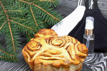 Baked cinnabons in shape. Stand on black pine planks. Nearby are spruce branches, medical masks and an antiseptic.