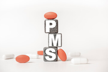 a group of white and red pills and cubes with the word PMS Premenstrual syndrome on them, white background. Concept carehealth, treatment, therapy.