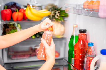 A girl opens a bottle of pink vegetable or fruit juice or homemade yogurt against the background of...