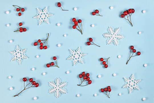 Seasonal red winter berries and white snowflake and snowball ornaments on light blue background 