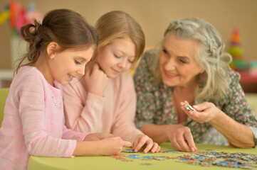 Fototapeta premium Portrait of grandmother with little granddaughters collecting puzzle