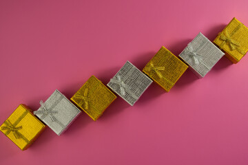 gift boxes of golden and silver color lie on a pink background.