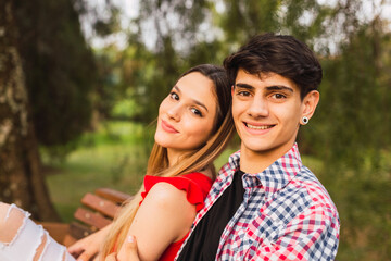 Obraz premium Portrait of a beautiful, smiling girl and her handsome boyfriend - Young couple sitting on a bench and smiling at the camera.