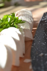 Marbel knife with chopped champignons with parsley on chopped wooden background. Backstage of cooking homemade spaghetti pasta alla carbonara with cheese and cream sauce. Sunny background. Close-up.