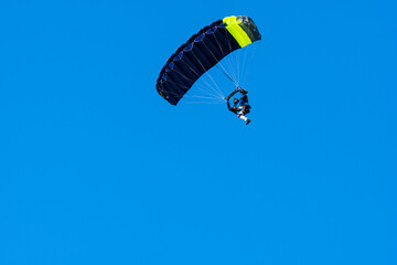 Tandem parachute jump. Silhouette of skydiver flying in blue clear sky