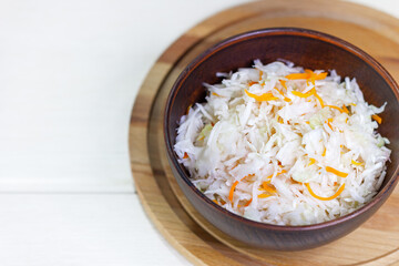 Sauerkraut with carrots in bowl on wooden background with copy space. Marinated vegetables.